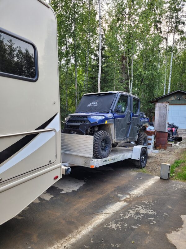 An all aluminum trailer with a front rock guard loaded with an UTV and being pulled by an RV.