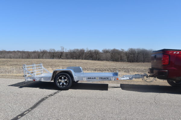 An all aluminum trailer with a bi fold ramp being pulled by a truck.