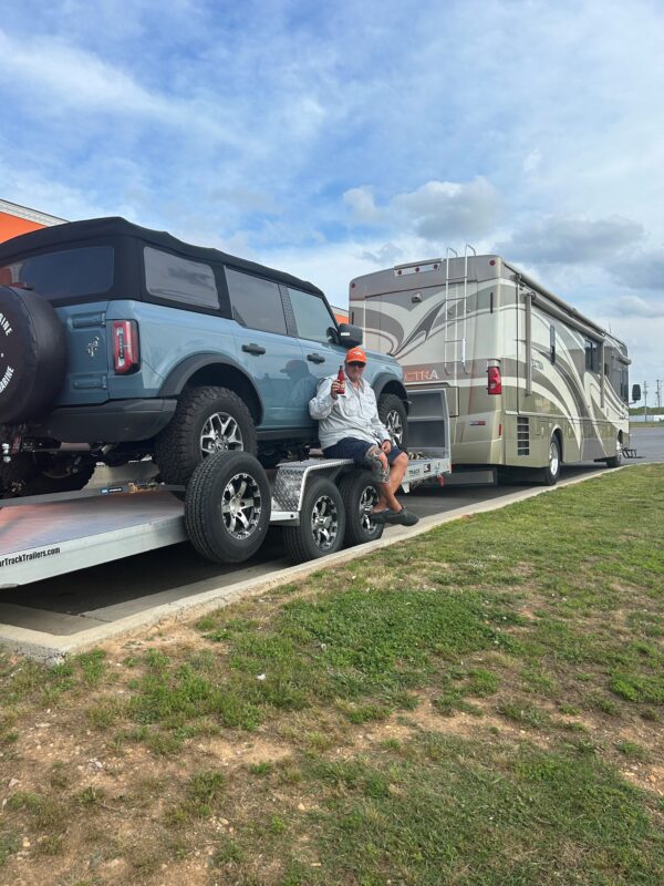 An all aluminum tilt car hauler loaded with a suv and being pulled by an RV.