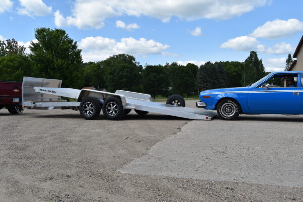 An all aluminum tilt car hauler in the tilted position. A blue car is about to drive onto the trailer.