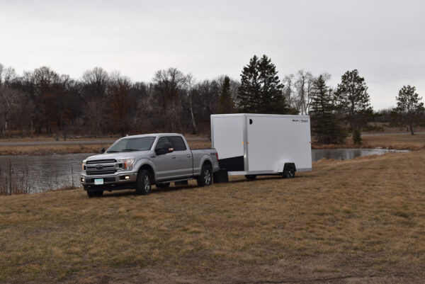 A single axle white enclosed trailer being pulled by a truck.