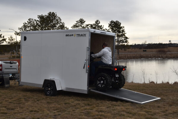 A man on an ATV driving into a single axle white enclosed trailer.