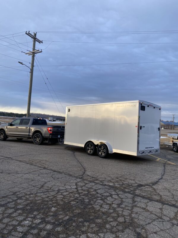 The rear door of a tandem axle white enclosed trailer hooked up to a truck.